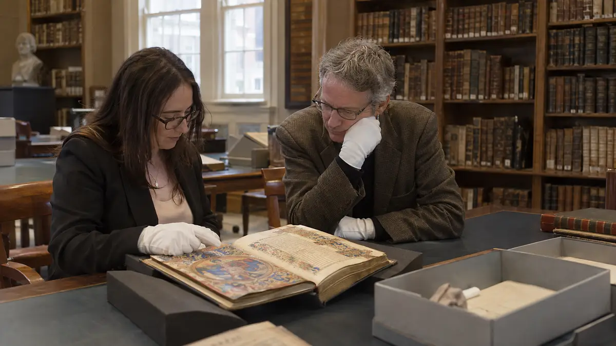 Researchers examining an illuminated manuscript in a historic library